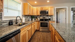 Una cocina moderna con gabinetes de madera, encimeras de granito y electrodomésticos de acero inoxidable, incluyendo un lavavajillas.