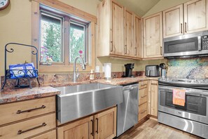 A kitchen with wooden cabinets, stainless steel appliances, a granite countertop, and a window with flowers. - Private Hot Tub - Huge Covered Deck- Garage - On Ski Bus Route (Steamboat Springs)