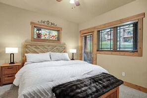 A bedroom with a bed, two bedside tables, a nightstand, a window with blinds, a ceiling fan, and a wall-mounted picture frame. - Private Hot Tub - Huge Covered Deck- Garage - On Ski Bus Route (Steamboat Springs)