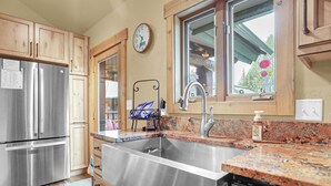 A kitchen with stainless steel appliances, wooden cabinets, a granite countertop, a sink, and a window with a view of greenery.