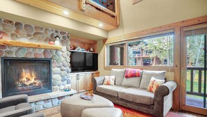 A cozy living room with a stone fireplace, a television, and a sofa with cushions.
