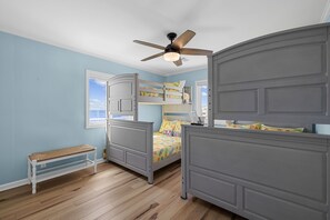 Ein Schlafzimmer mit Etagenbett, einem Einzelbett, Deckenventilator, einer Bank und einem Fenster mit Blick auf den Himmel.