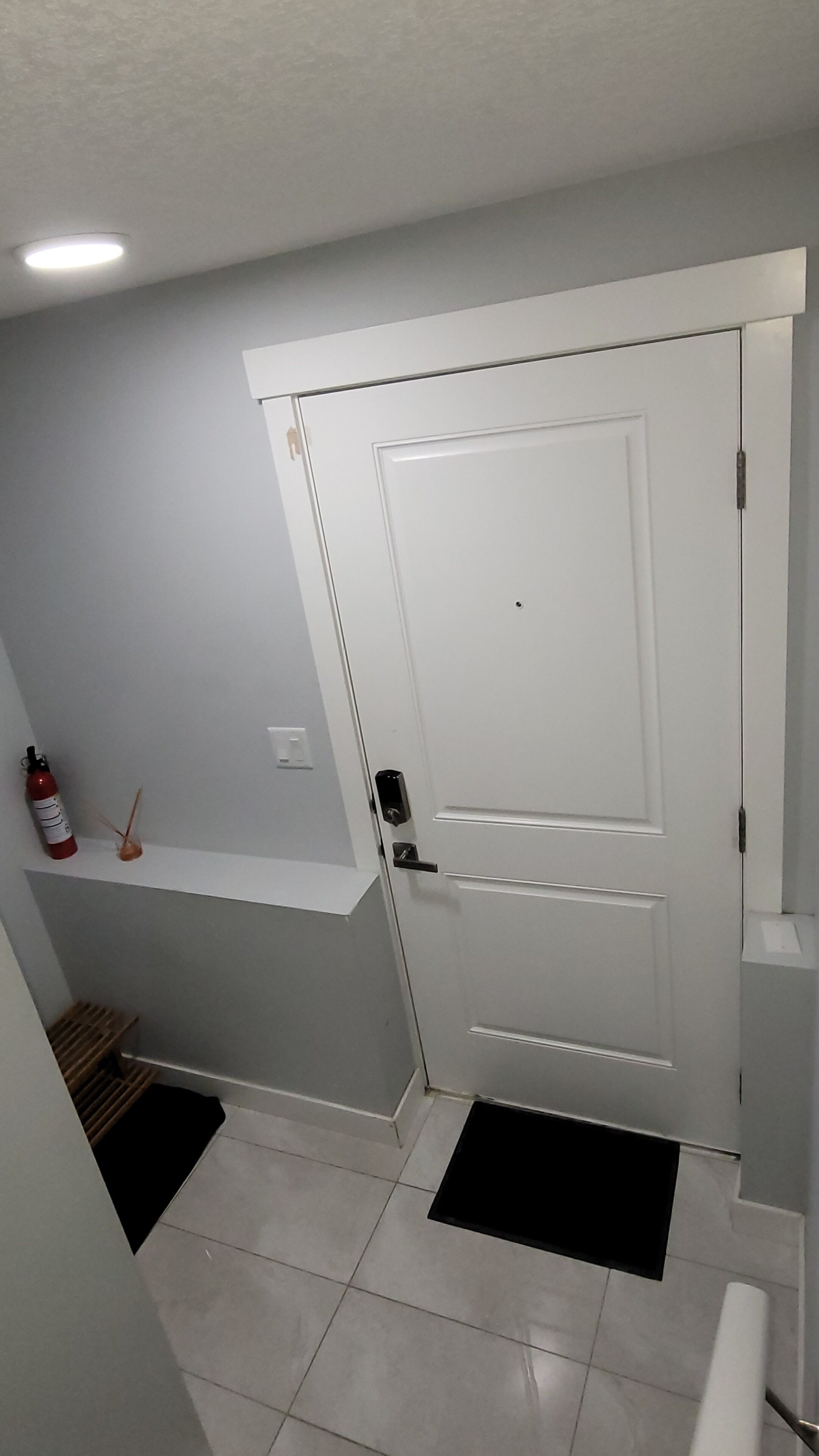 A hallway with a white door, a fire extinguisher, and a small shelf.