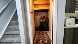 A narrow hallway with a wooden ceiling and a carpeted floor leading to a small room with a washing machine and a radiator. - Luxurious home away from home with AC in a quiet & Clean Neighborhood just 4 U (Airdrie)