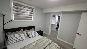 A bedroom with a bed, bedside table, lamp, and a window with blinds. - Luxurious home away from home with AC in a quiet & Clean Neighborhood just 4 U (Airdrie)