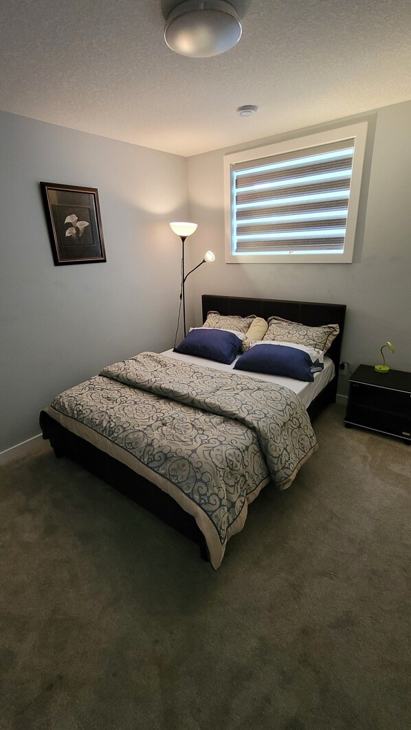 A bedroom with a bed, a floor lamp, a window with blinds, a picture on the wall, and a ceiling light. - Luxurious home away from home with AC in a quiet & Clean Neighborhood just 4 U (Airdrie)