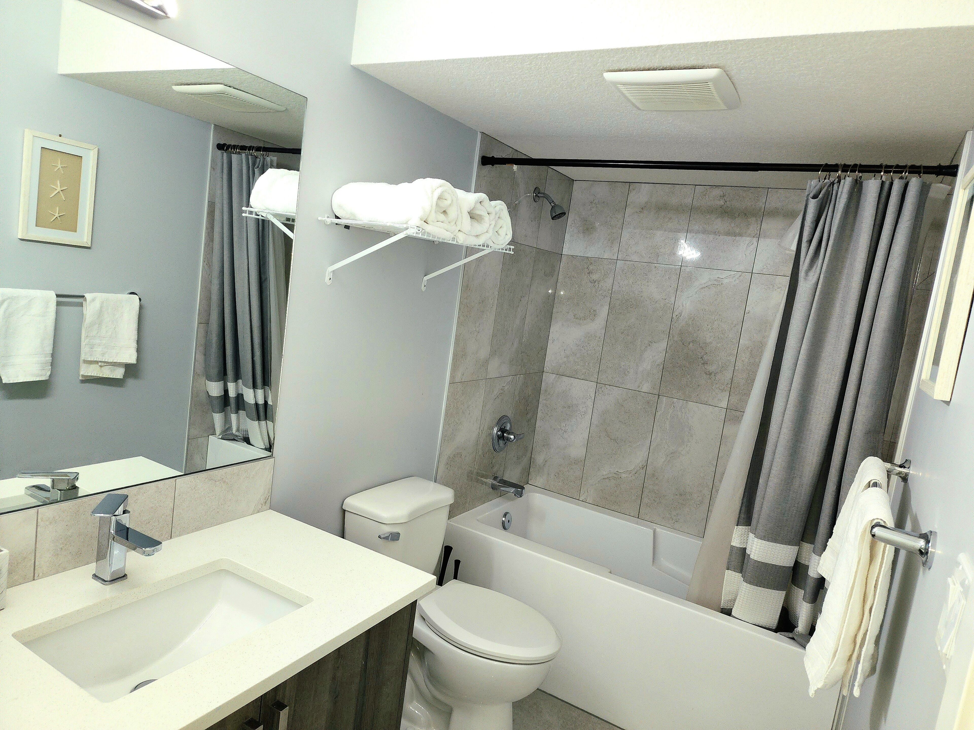 A modern bathroom with a sink, toilet, bathtub, and shower curtain.