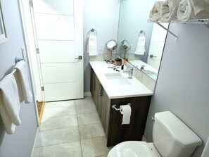 A bathroom with a toilet, sink, mirror, towel rack, and a door. - Luxurious home away from home with AC in a quiet & Clean Neighborhood just 4 U (Airdrie)