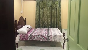 A single bed with a patterned bedspread, a white pillow, and a green curtain. - Superb apartment with AC located on the public road seawall (Georgetown)