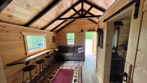 Un intérieur de chalet chaleureux avec un plafond en bois, un canapé, un coin bar avec des tabourets et un tapis à motifs.