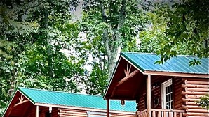 Deux cabanes en bois aux toits verts, chacune dotée d’une véranda et d’une fenêtre.