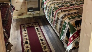 Une chambre dans une cabane en bois, avec un lit, une table de chevet avec une lampe, un tableau encadré au mur et une échelle en bois.