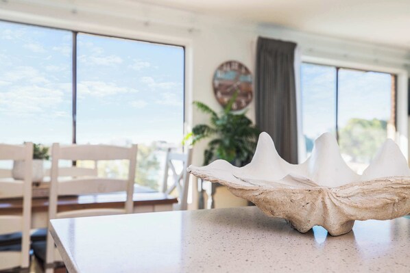 A table with a unique shell-shaped centerpiece, a white chair, and a view of the outdoors through large windows.