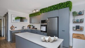 A modern kitchen with grey cabinetry, a central island, a built-in oven, and a stainless steel refrigerator.