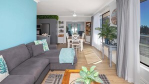 A modern living room with a gray sofa, a coffee table, and a dining area with a white table and chairs.
