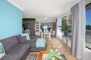 A modern living room with a gray sofa, a coffee table, and a dining area with a white table and chairs. - BJ Mick's Lakefront Apartment - Central Forster (Forster)