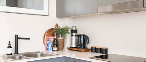 Una cocina moderna con gabinetes grises, un lavamanos de acero inoxidable, una cafetera y una planta en la encimera.