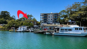 A marina with docked boats, a building with balconies, and lush greenery.