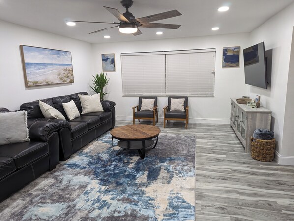 A modern living room with a black leather sofa, two armchairs, a coffee table, and a large window with blinds. - Spacious Lake House retreat located in Clearwater FL, near beaches & shopping. (Clearwater)