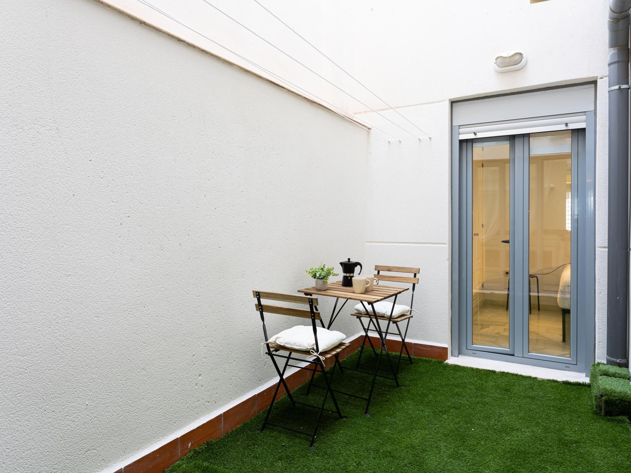 Un petit espace extérieur aménagé avec une table et des chaises, une cafetière et une plante en pot.