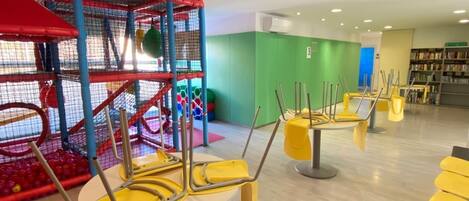 A children's play area with a climbing structure and yellow chairs arranged for seating.