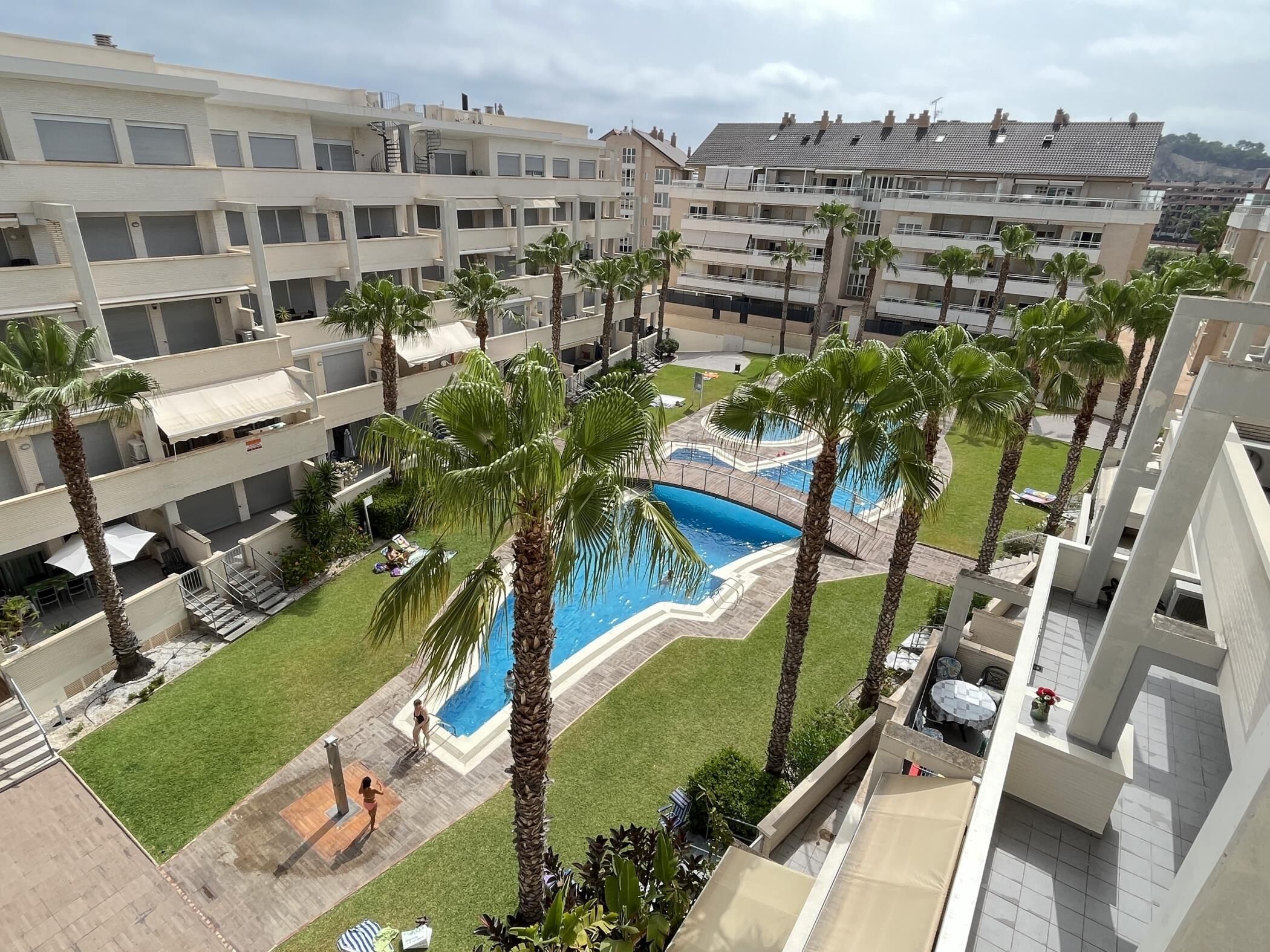 Un hotel a più piani con piscina centrale circondata da palme e un prato curato.