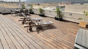 Eine Dachterrasse mit Holzboden, Liegestühlen und Topfpflanzen.