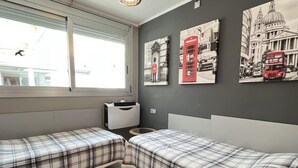 Ein Zimmer mit zwei Betten, einem Fenster und Wandbildern, die Londoner Sehenswürdigkeiten zeigen.