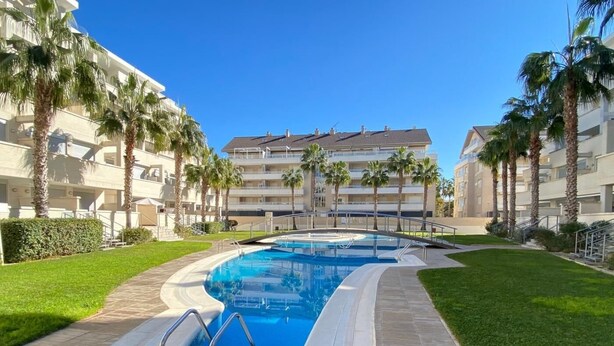 Ein Pool mit einer gefliesten Liegefläche, umgeben von Palmen und einem Gebäude mit mehreren Balkonen.