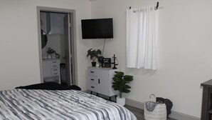 A bedroom with a bed, a dresser, a TV, a plant, and a basket.