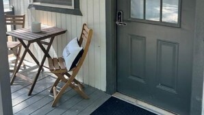 Eine hölzerne Veranda mit einer dunkelgrünen Tür, einem kleinen Tisch und einem Stuhl.