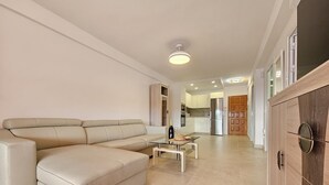 A spacious living room with a large beige sectional sofa, a glass coffee table, and a kitchen area in the background. - Heart of Los Cristianos,Heated Pool (Los Cristianos)