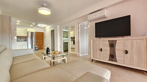 A modern living room with a sofa, a glass coffee table, a TV on a wooden cabinet, and an open kitchen in the background. - Heart of Los Cristianos,Heated Pool (Los Cristianos)
