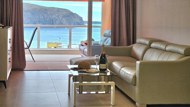 A room with a leather sofa, a glass coffee table, and a view of the sea through large windows. - Heart of Los Cristianos,Heated Pool (Los Cristianos)