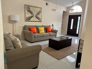 Una sala de estar con un sofá, sillones, una mesa de centro, una lámpara, un cuadro y una puerta con ventana.