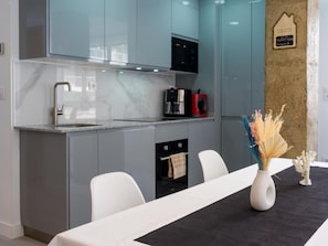 A modern kitchen with grey cabinets, a stainless steel range hood, and a dining area with a white table and chairs.