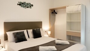 A neatly made bed with a brown headboard, a bedside table with a lamp, and a wardrobe with a hanging garment. - Apartamento playa Cullera (Cullera)
