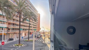 A balcony with a view of a street, palm trees, and a building with balconies. - Apartamento playa Cullera (Cullera)