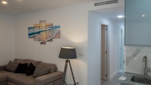 A modern living room with a sofa, a floor lamp, a wall art piece, and a kitchen area with a sink. - Apartamento playa Cullera (Cullera)