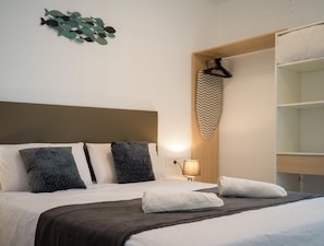 A neatly made bed with pillows, a bedside lamp, and a wall-mounted shelf with a towel.