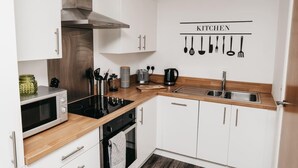 Une cuisine moderne avec des armoires blanches, une hotte de cuisinière en acier inoxydable, un four à micro-ondes, une bouilloire et un évier.