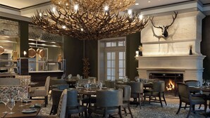 A dining area with tables set for guests, a fireplace, and a mounted deer head on the wall.
