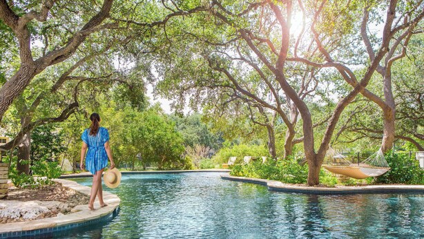 A pool area with a person standing on a platform, surrounded by trees and greenery.