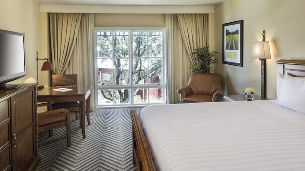A hotel room with a large bed, a desk with a chair, a television, and a window with curtains. - 1-Bedroom Suite at a 4⭐️ Hotel (San Antonio)