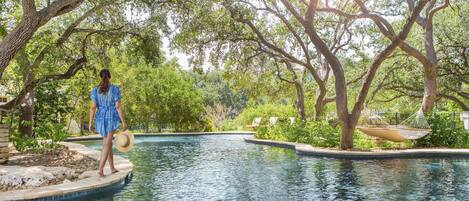 A pool area with a person standing on a platform, surrounded by trees and a hammock.