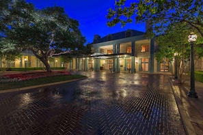 A hotel entrance with a brick pathway, large windows, and a tree in the foreground.