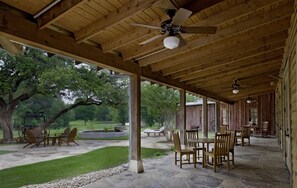 A covered outdoor patio with a ceiling fan, wooden furniture, and a view of a grassy area with trees. - 1-Bedroom Suite at a 4⭐️ Hotel (San Antonio)