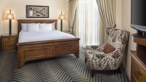 A hotel room with a large bed, two bedside lamps, a patterned armchair, a television, and a decorative wall piece. - 1-Bedroom Suite at a 4⭐️ Hotel (San Antonio)