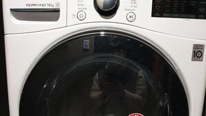 Vista frontal de uma máquina de lavar LG TROMM, com visor digital, painel de controle e porta transparente.