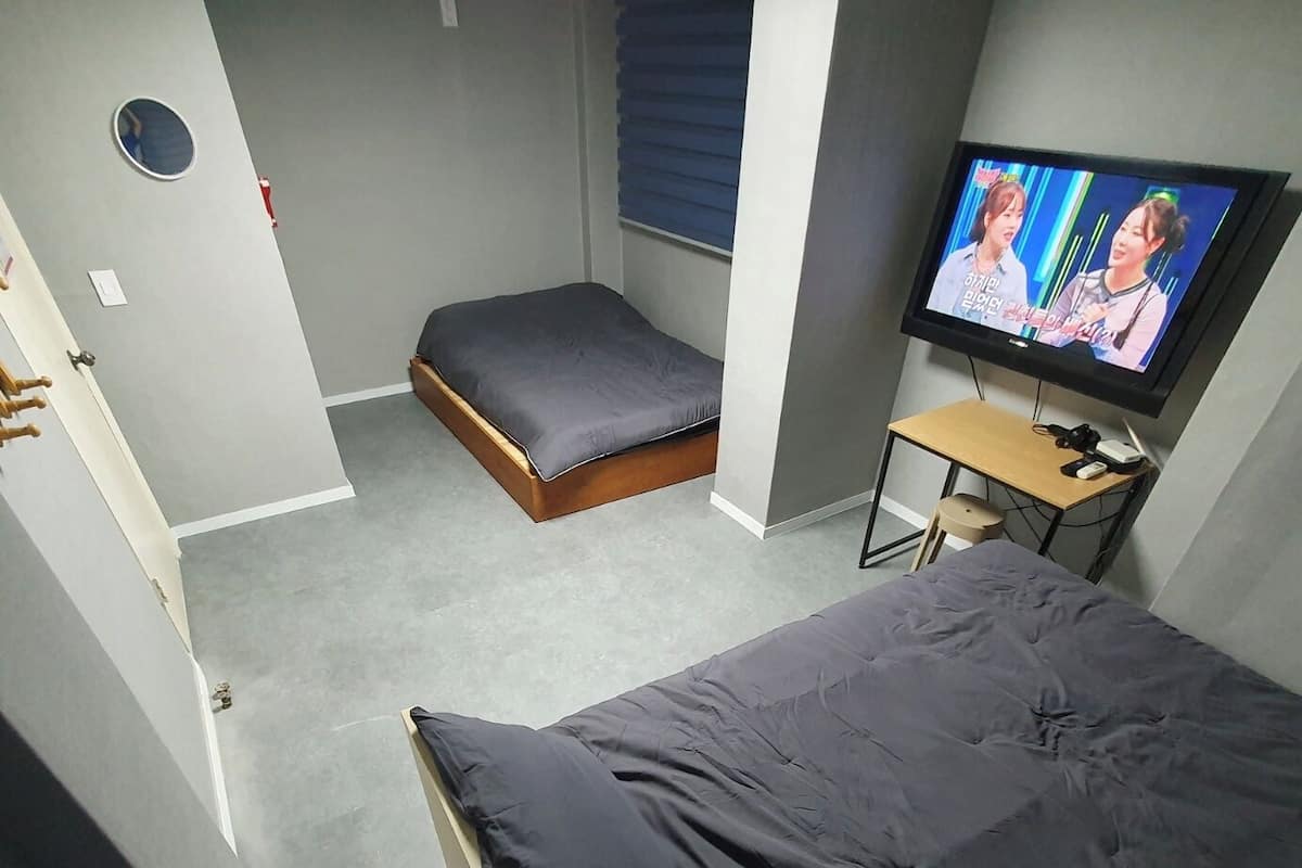 A bedroom with a bed, a small seating area, a television, and a window.